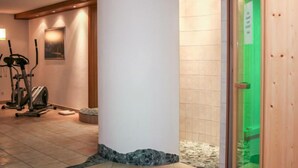 Un hall d’hôtel avec une grande colonne blanche, du matériel de musculation et une porte en verre vert.