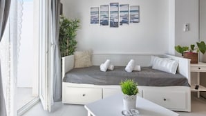 A modern, minimalist bedroom with a white sofa bed, a small table, and a potted plant.