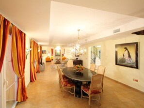 A spacious dining area with a round table and chairs, a chandelier, and a staircase leading to an upper level.