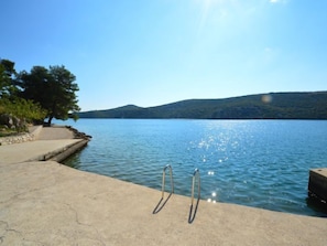 A concrete pier extending into a calm lake with a clear sky and distant hills.