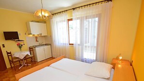 Een hotelkamer met een tweepersoonsbed, een bureau met stoel, een kleine kitchenette en een televisie aan de muur.