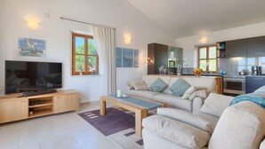 A modern living room with a flat-screen TV, a sofa, a coffee table, and a kitchen area with cabinets and a stove. - Vacation home Nini by Interhome (Buje)