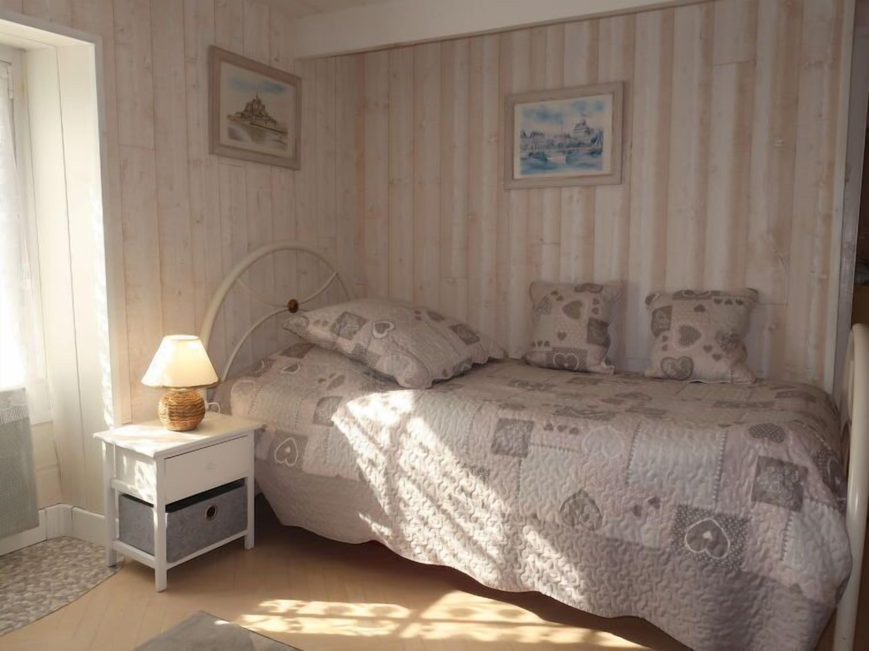 Een slaapkamer met een bed, nachtkastje en twee foto’s aan de muur.