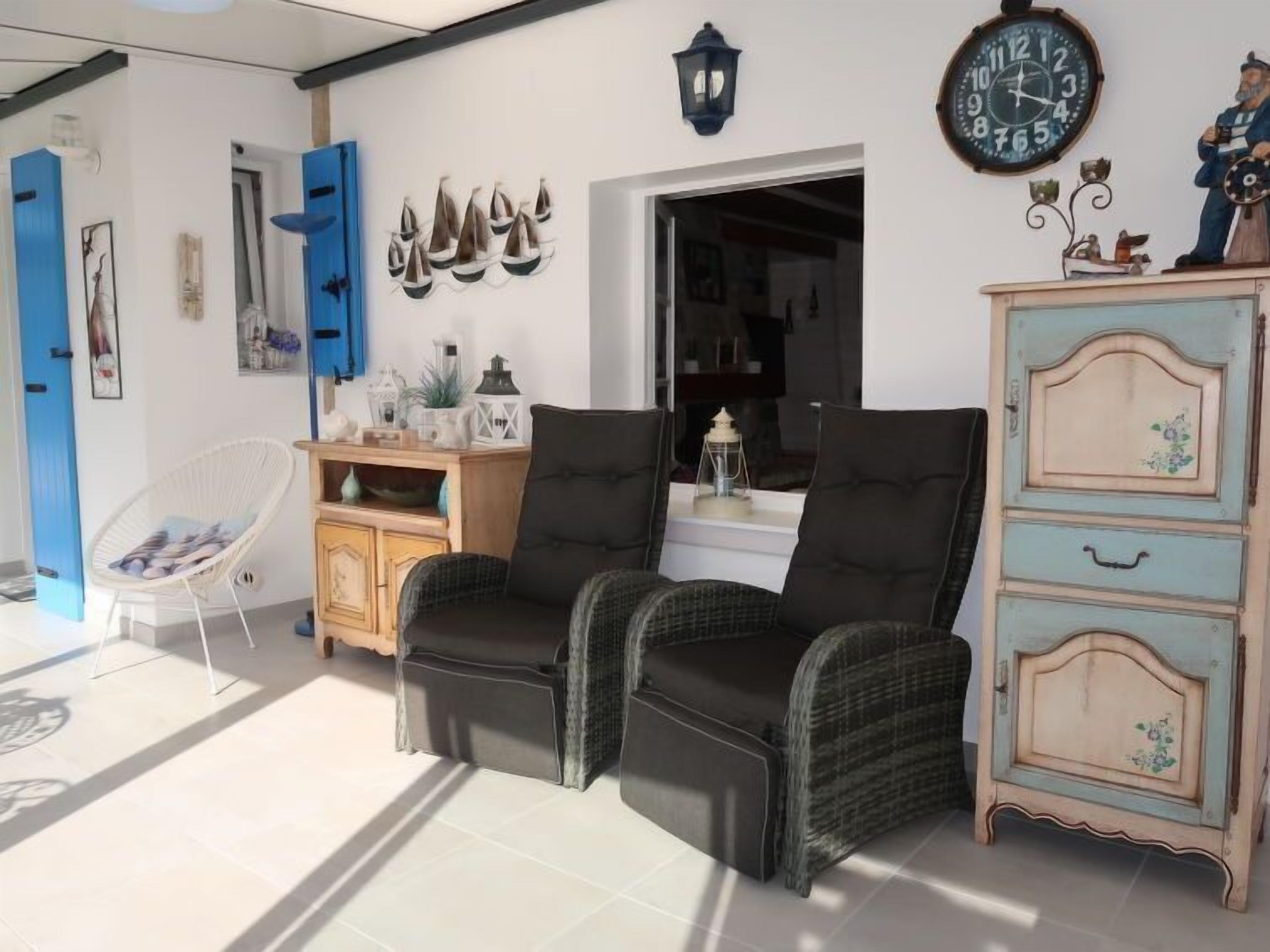 A room with two black upholstered chairs, a wooden cabinet with drawers, a blue door, and a wall clock.