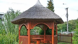 Un kiosque en bois avec un toit de chaume, entouré de verdure.
