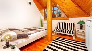 Une chambre mansardée chaleureuse, avec un plafond en bois incliné, un lit avec une literie à rayures, une petite chaise, une lampe et un radiateur.
