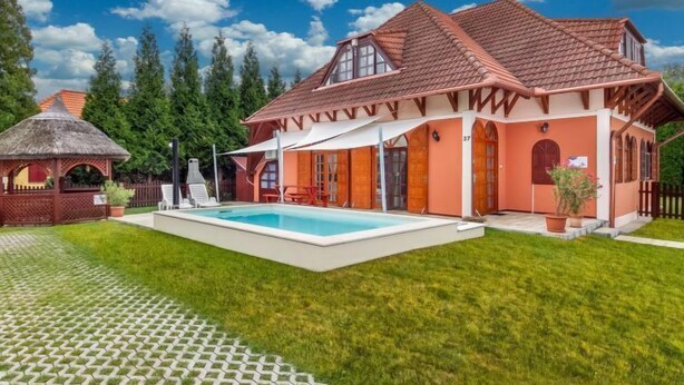 Une maison avec une piscine, un belvédère au toit de chaume et une pelouse bien entretenue.