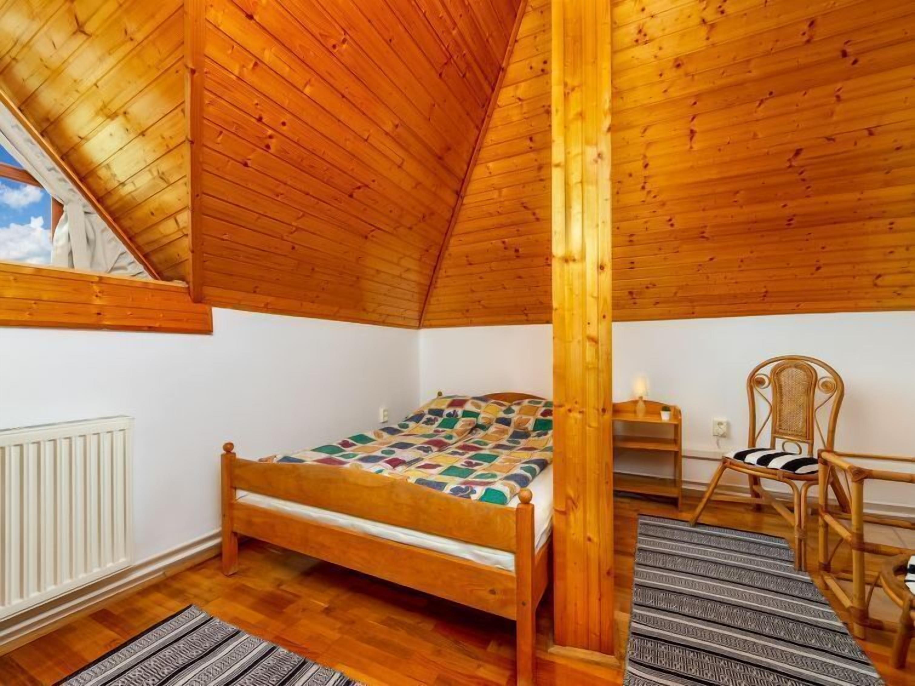 Une chambre mansardée chaleureuse avec un plafond en bois, un lit simple, une chaise et une petite table.