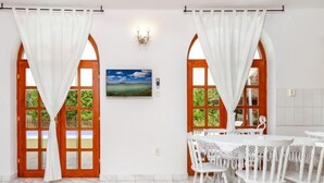 Un coin repas avec des chaises blanches et une table, deux portes en bois dotées de panneaux de verre, et un tableau accroché au mur.