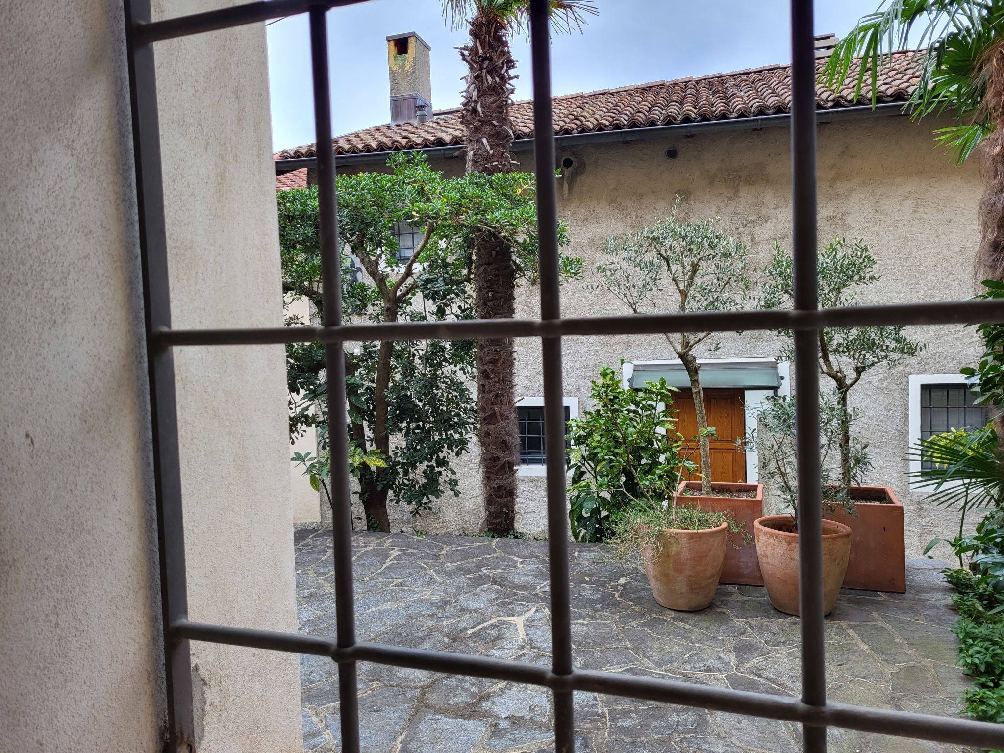 A courtyard with stone flooring, potted plants, and a building with a tiled roof.