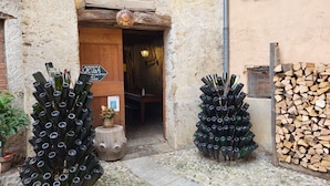 Un edificio rústico con una puerta de madera y un letrero que dice “Grotto di Porti”. Hay dos grandes arreglos de botellas de vino afuera, y una pila de leña a la derecha.
