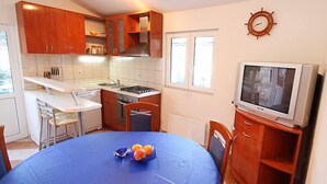 Una cocina compacta con armarios de madera, una mesa de comedor con mantel azul, un televisor pequeño y un reloj en la pared.