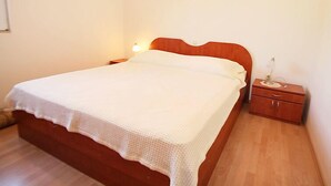 Una cama individual con cabecera de madera, una mesita de noche con lámpara, y un pequeño mueble de madera.