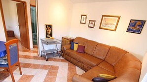 Un salón con un sofá de cuero marrón, una silla azul y una pequeña mesa con una bandeja. Hay cuadros enmarcados en la pared y una puerta que da a otra habitación.