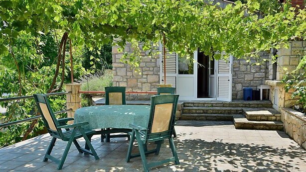 Un patio al aire libre con una mesa y sillas, rodeado de muros de piedra y follaje.