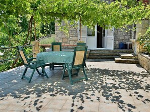 Un patio al aire libre con una mesa y sillas, rodeado de muros de piedra y follaje.
