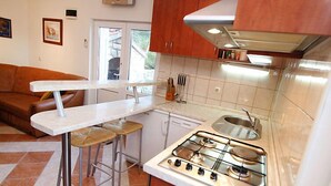 Una cocina pequeña con estufa a gas, un lavamanos y un taburete de bar. Se ve una ventana con vistas al exterior.