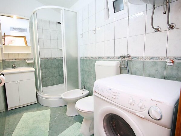 Un baño con ducha, inodoro y lavadora.