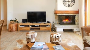 Een woonkamer met een open haard, een televisie en een klok aan de muur.