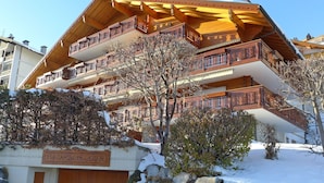 Een houten chalet met meerdere verdiepingen, balkons, een stenen muur en een bord met de tekst 'LES CASCADES D'EDEN'.