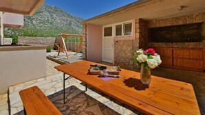 A patio with a wooden table, a bench, and a stone floor. There is a stone wall and a view of mountains in the background. - Apartment Golub by Interhome (Karlobag)