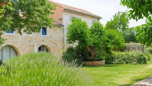 Un edificio in pietra con finestre ad arco e un giardino con erba alta e alberi.