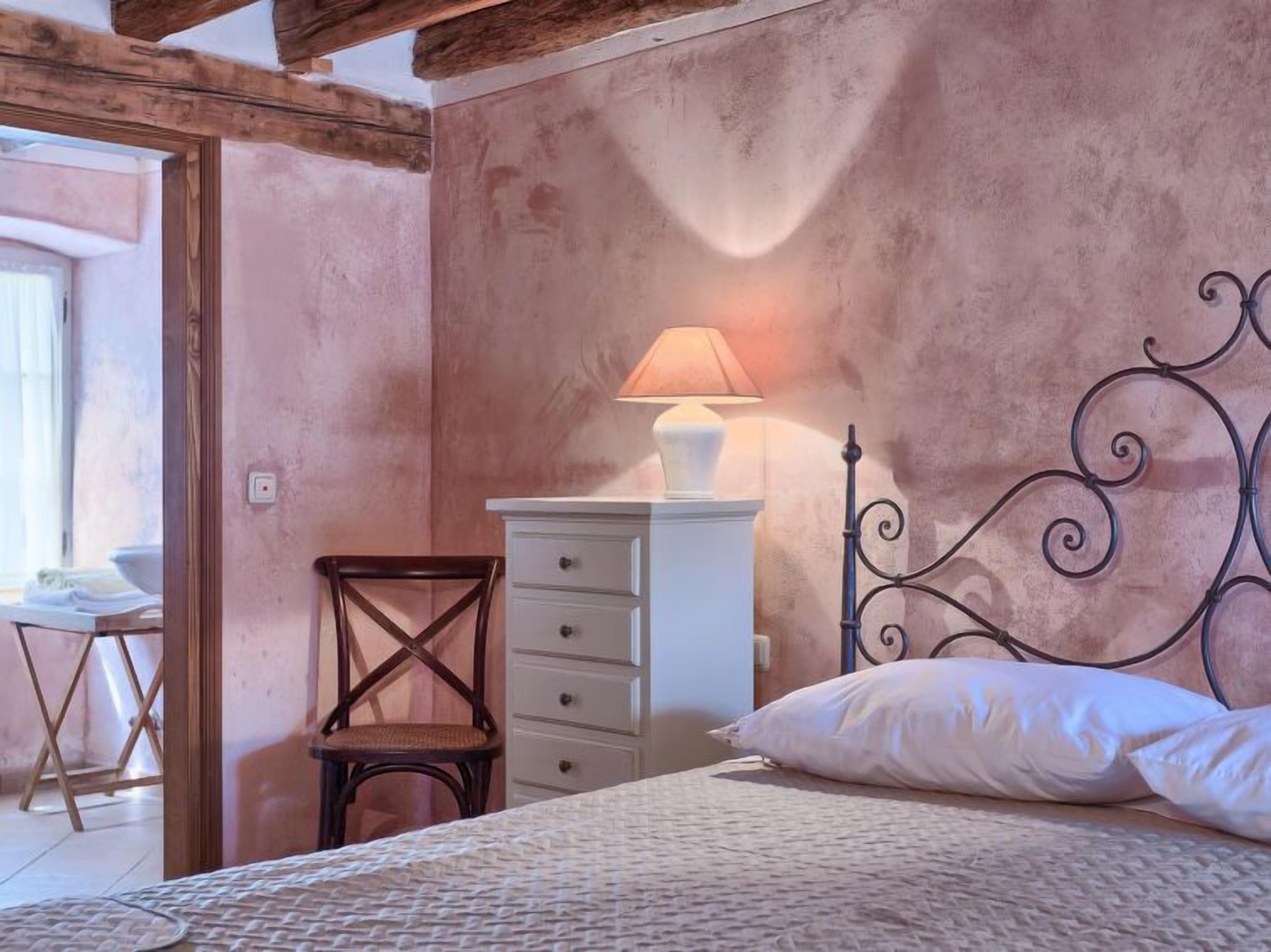 A bedroom with a bed, a wooden chair, a white dresser, and a lamp.