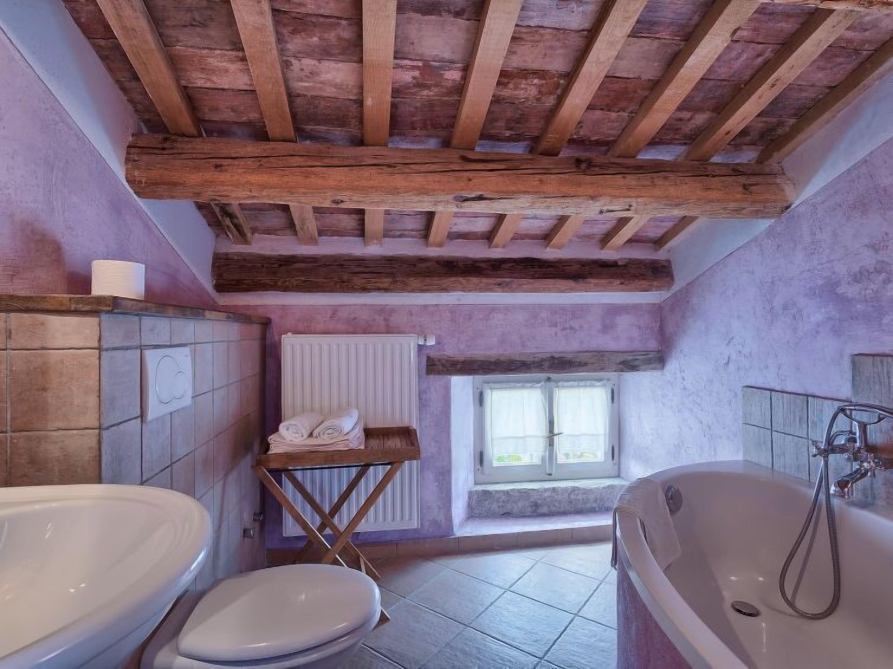 A bathroom with a wooden ceiling, a window, a bathtub, and a toilet.