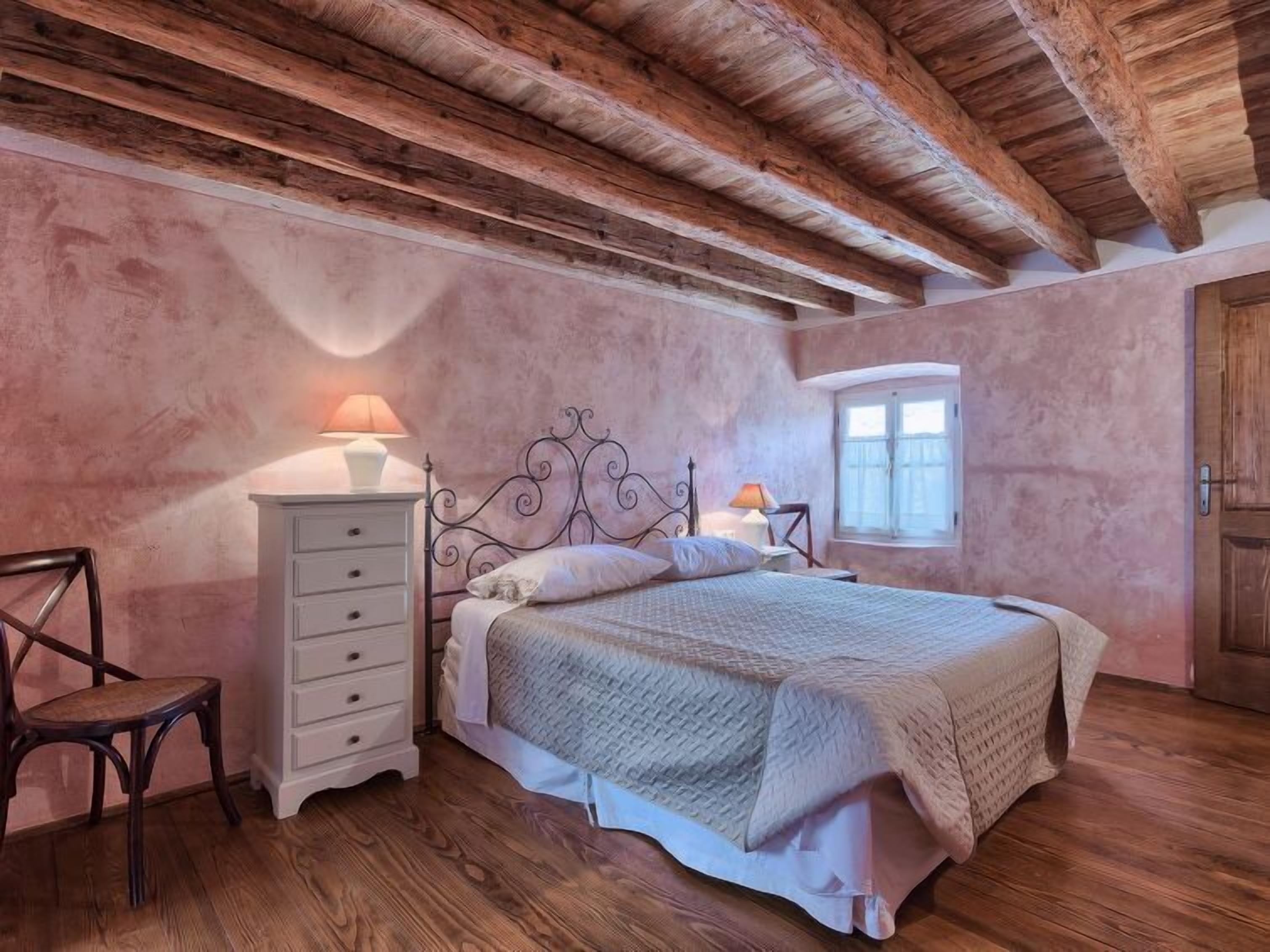 Ein Schlafzimmer mit Holzboden, einem Bett mit Kopfteil, einem Nachttisch, einem Stuhl und einem Fenster.