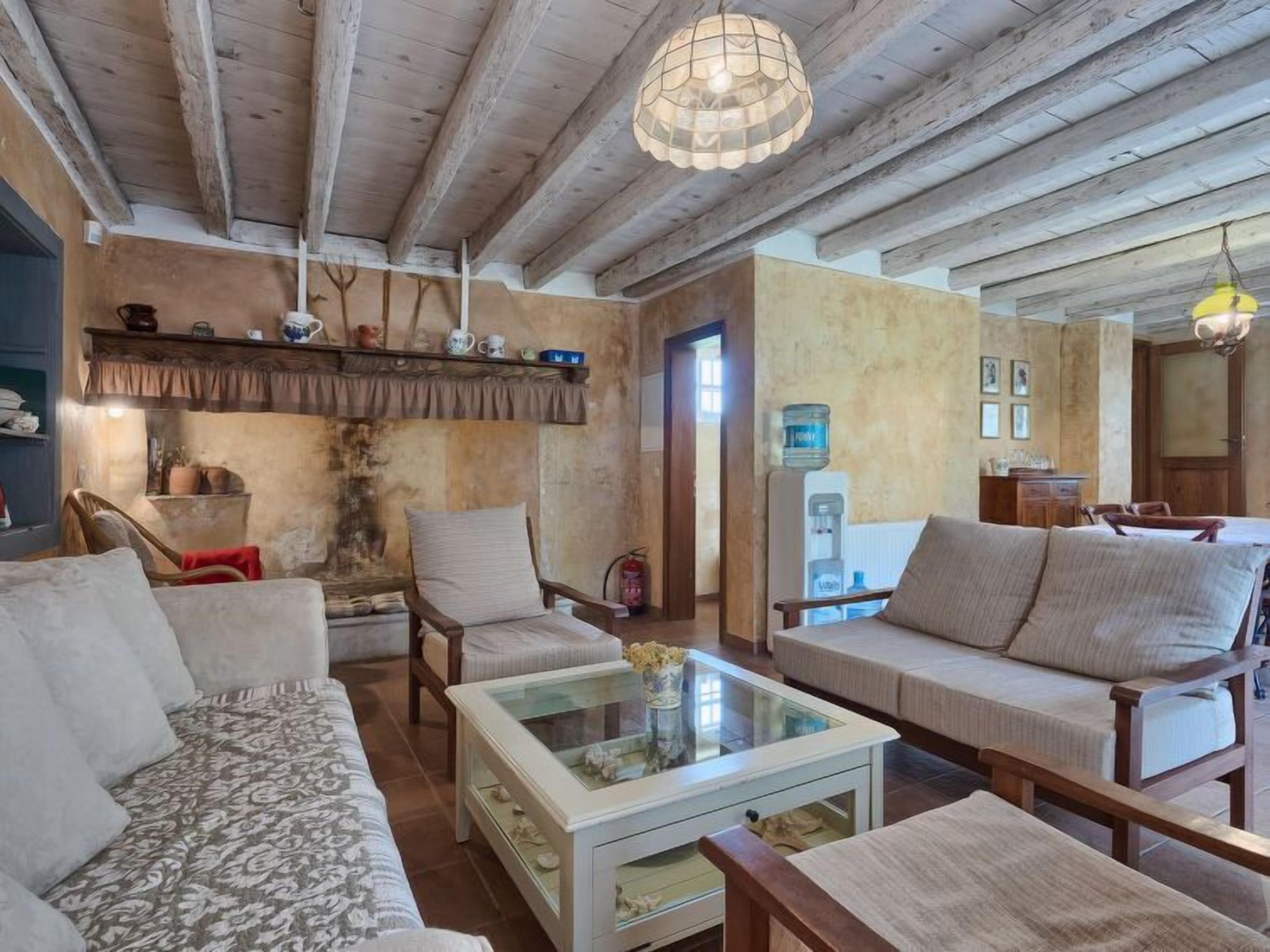 Una sala rústica con vigas de madera a la vista, una mesa de centro de vidrio y un sofá.