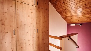 Een houten trap met een leuning, die leidt naar een kamer met een paarse wand en een houten plafond.