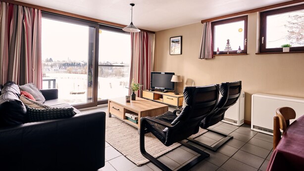 Een moderne woonkamer met een bank, een fauteuil, een televisie en een houten salontafel.