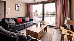 Een moderne woonkamer met een zwarte leren bank, een houten salontafel en zicht op een besneeuwd landschap door grote ramen.