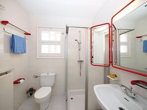 Un baño con inodoro, ducha y lavamanos, que incluye un espejo con marco rojo y una toalla azul.