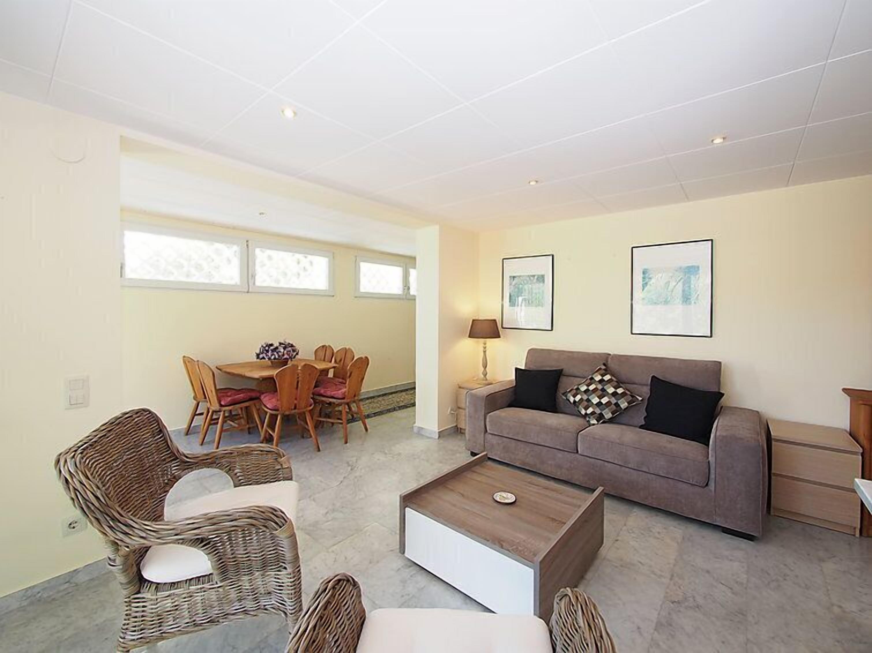 A living room with a grey sofa, wicker chairs, a coffee table, and a dining area with a table and chairs.