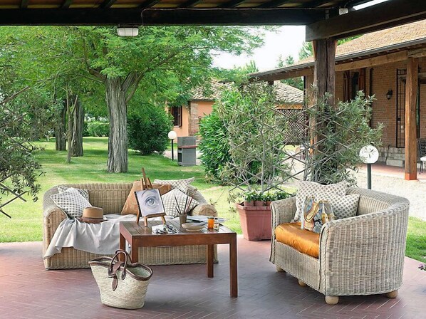 A covered outdoor seating area with wicker furniture, a table, and potted plants.