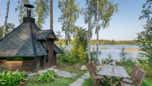 Een rustieke chalet met een stenen schoorsteen, een houten terras en een tafel met stoelen.