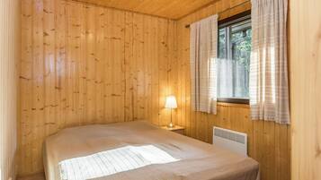 A wooden-paneled room with a bed, a window with curtains, and a wall-mounted heater.