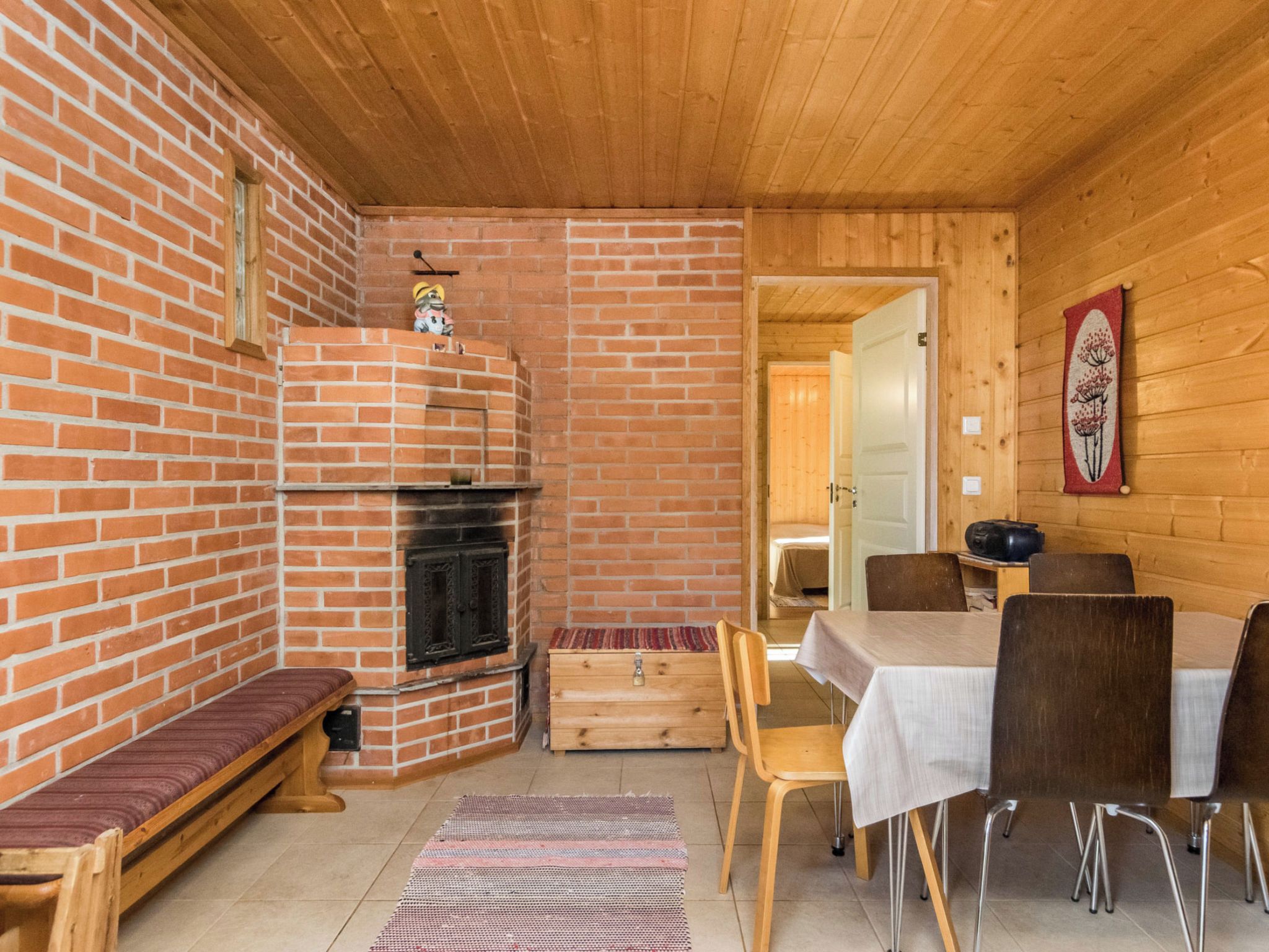 Una habitación acogedora con chimenea de ladrillo, paredes de madera, una mesa de comedor con sillas y un banco.