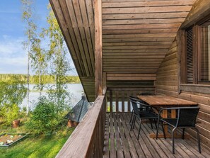 Une terrasse en bois avec une table et des chaises, donnant sur une étendue d’eau et une zone verdoyante.