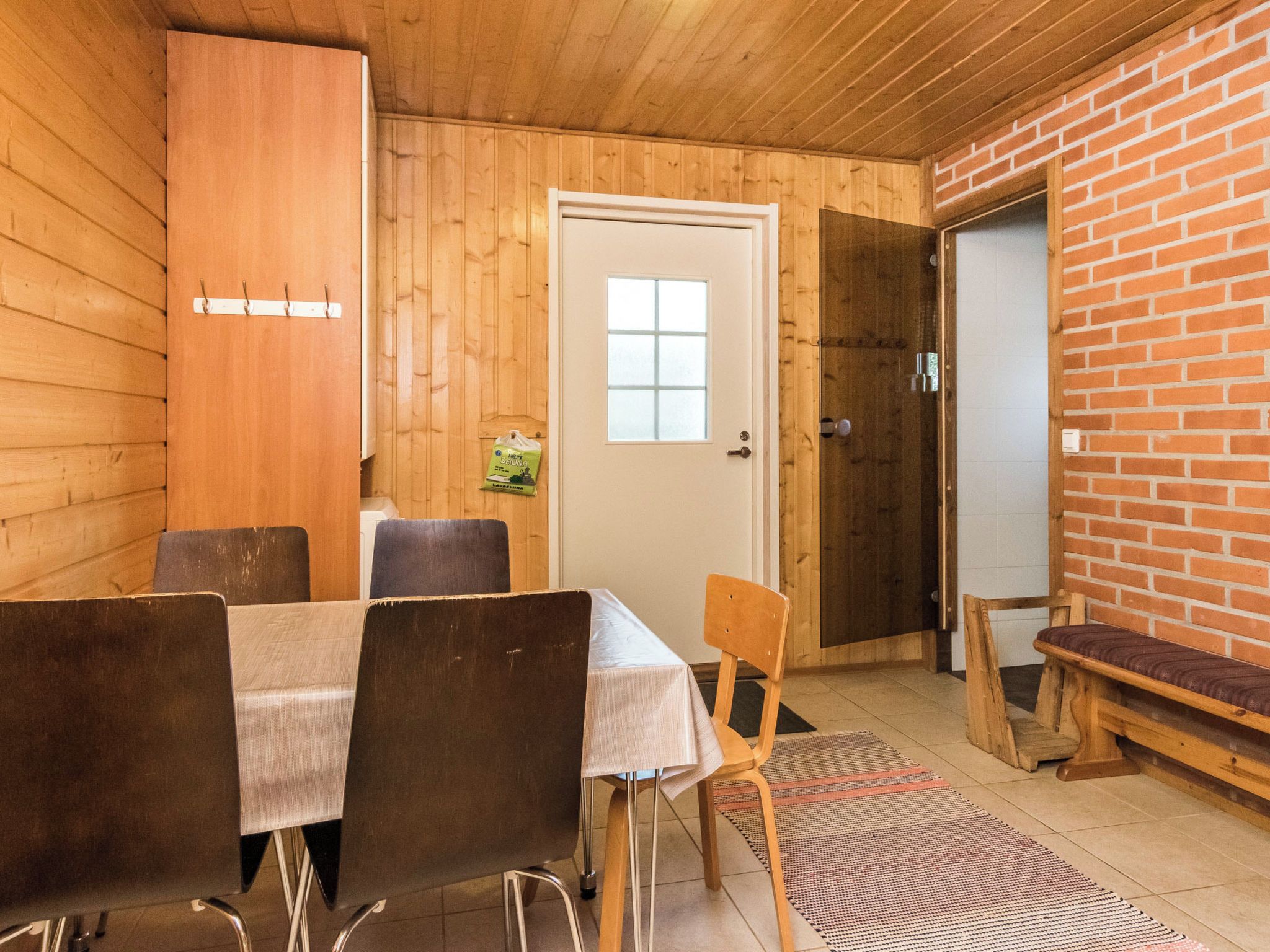 Puisesti sisustettu tila, jossa on ruokapöytä ja tuoleja, penkki, ovi ja tiiliseinä.