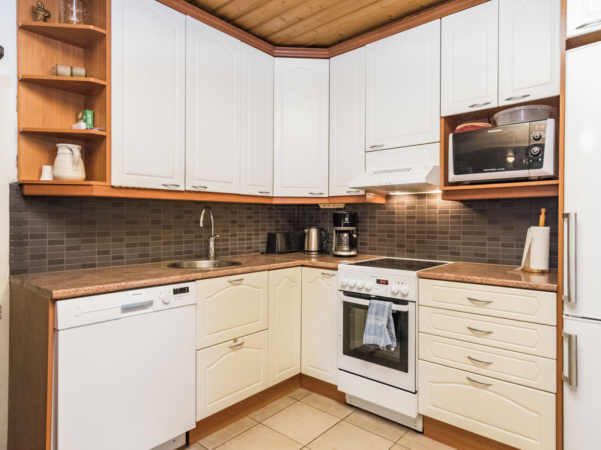 Une cuisine compacte avec des meubles blancs, un four à micro-ondes encastré, une cuisinière et un lave-vaisselle.