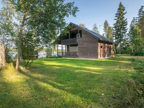 Une cabane en bois dotée d’un balcon, entourée d’une zone herbeuse et d’arbres.