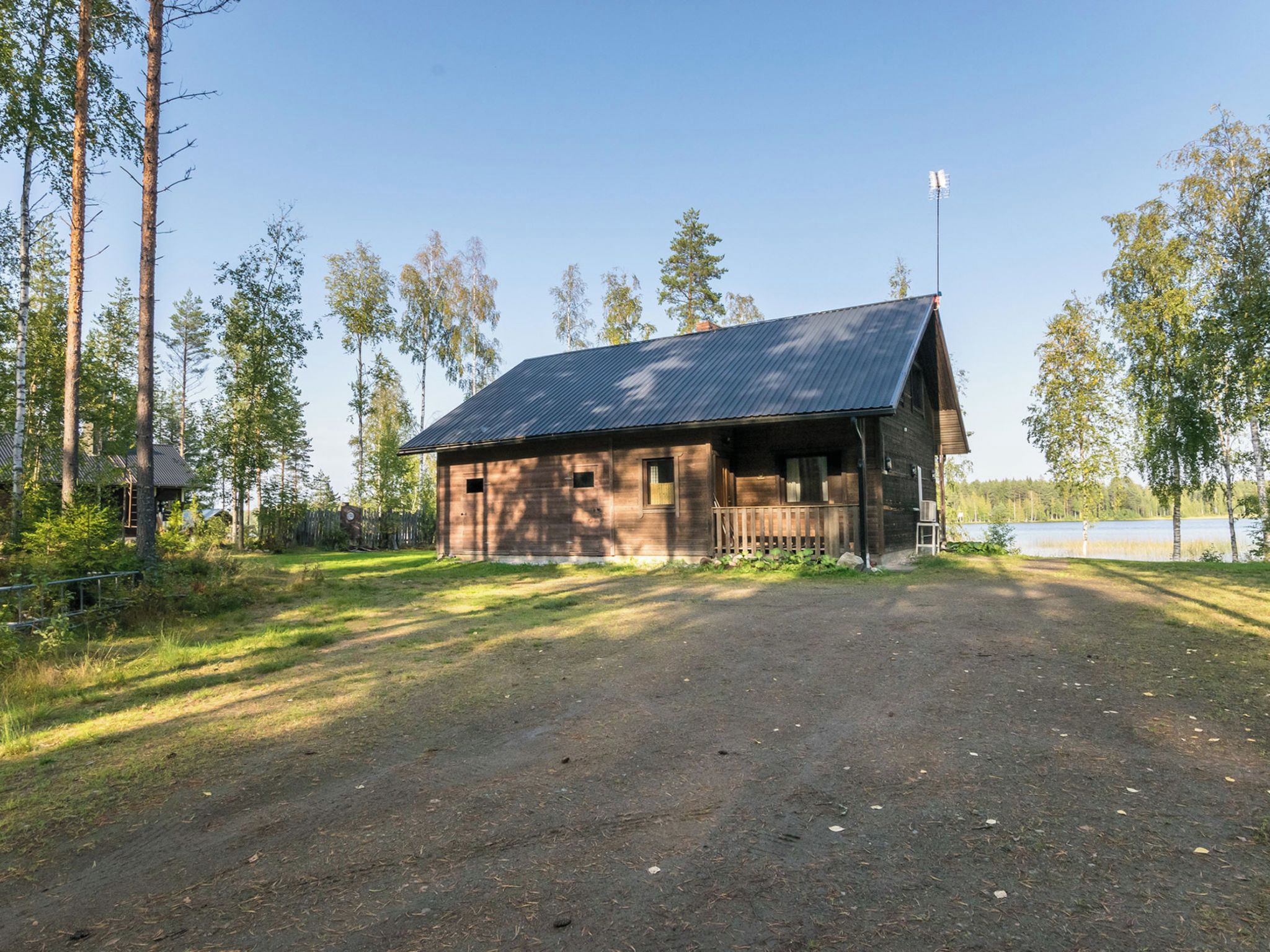 Eine rustikale Holzhütte mit einem Metalldach, umgeben von Bäumen und einem Feldweg.