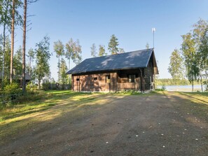 A rustic wooden cabin with a metal roof, surrounded by trees and a dirt path. - Aurinkopaikka by Interhome (Juva)