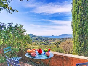 Mesa com vista para um vale e montanhas, um banco e uma mesa posta com chaleira e fruta.