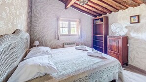 Et soveværelse med seng, træskab, ventilator og et vindue med gardiner.