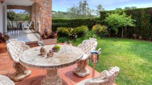 Une terrasse en pierre avec une table ronde et des chaises, entourée d’un jardin luxuriant et d’un mur de pierre.