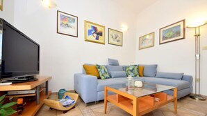 A living room with a sofa, a glass coffee table, a TV on a wooden stand, and a lamp.