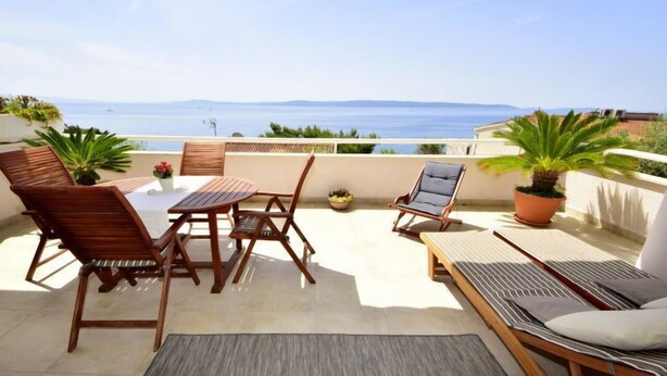 A terrace with a table and chairs, a lounge chair, and potted plants.